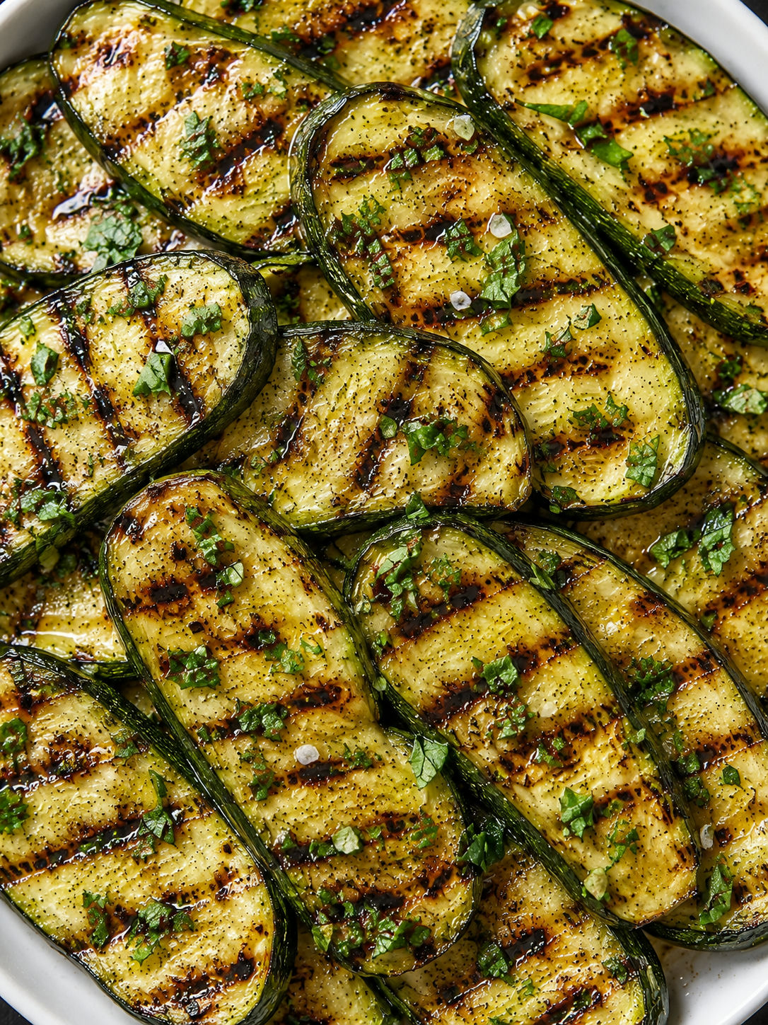 Top-down grilled zucchini brushed with oil, char marks and fresh basil