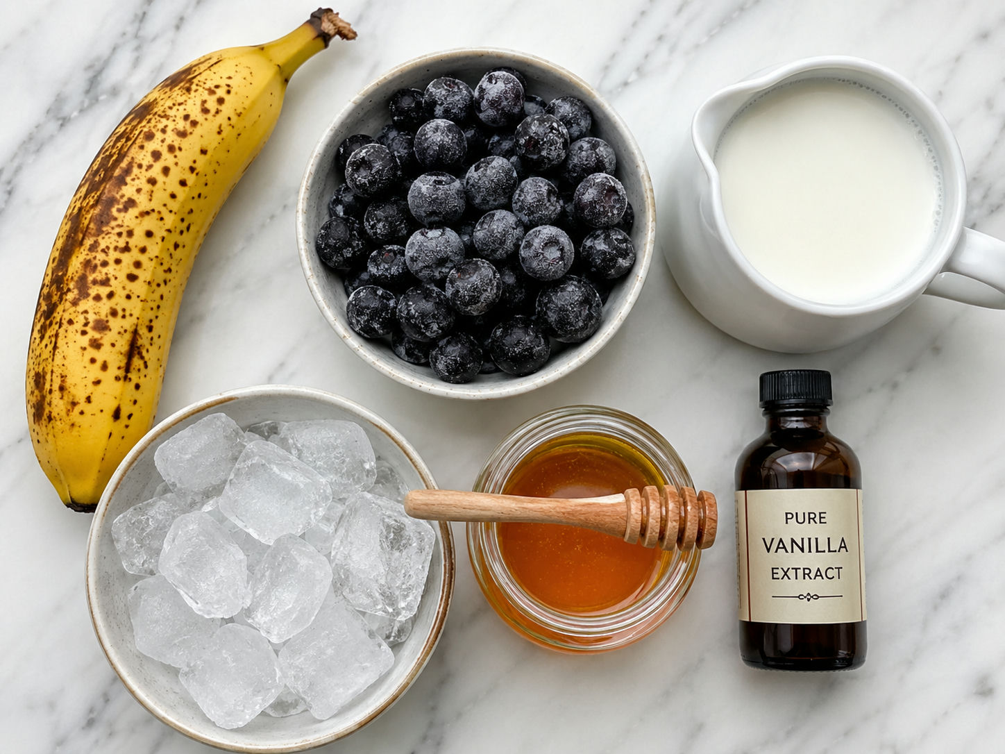 Banana blueberry frappuccino ingredients on marble with banana, blueberries, milk, ice, and honey