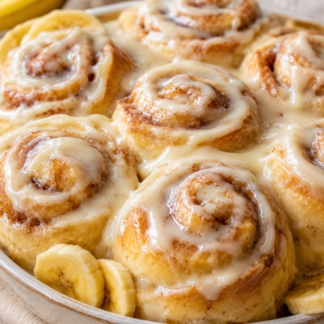Banana cinnamon rolls with cream cheese icing on a light wood board