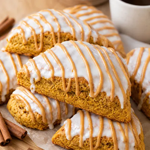 Pumpkin scones with white glaze and pumpkin spice drizzle on parchment