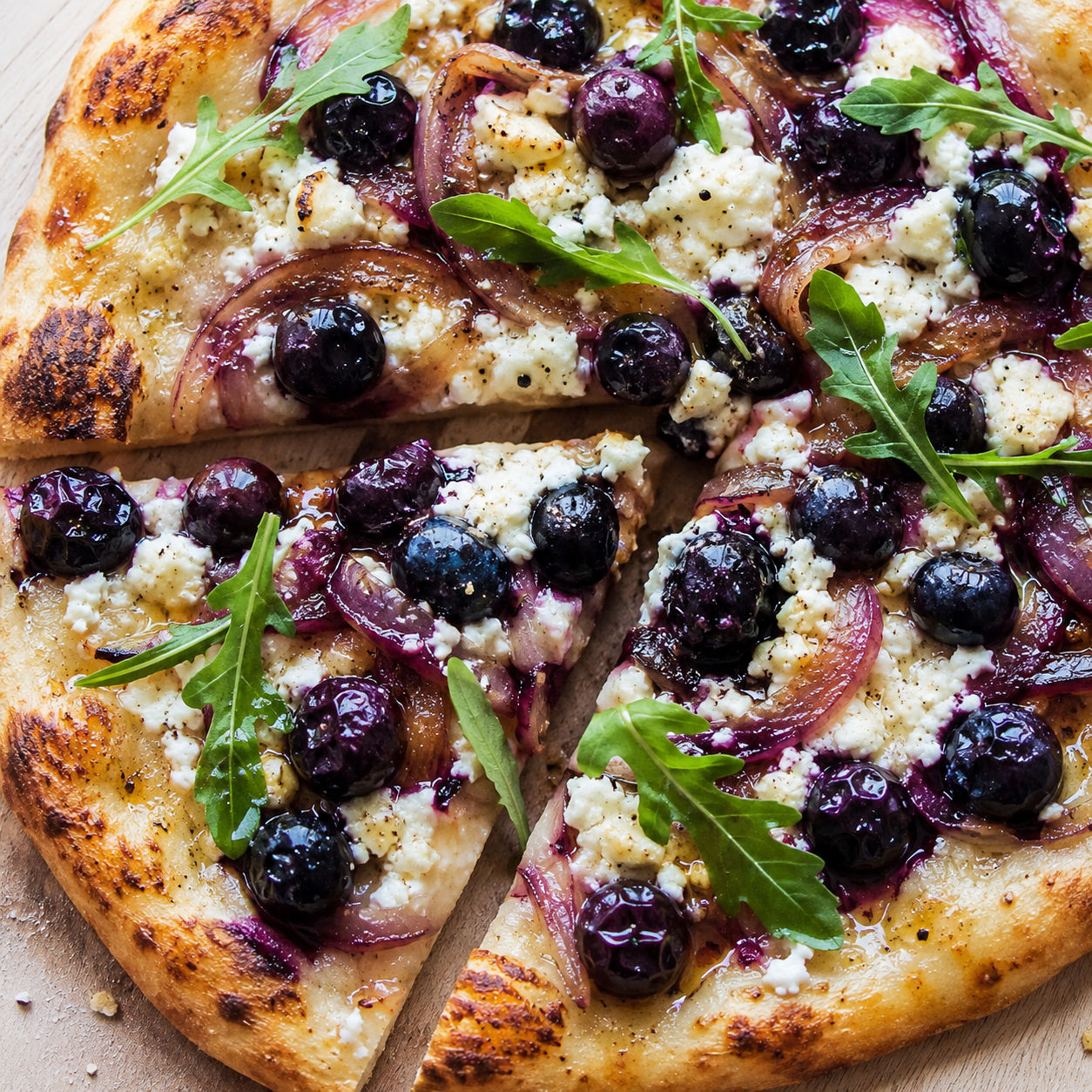 Blueberry feta honey naan pizza with arugula on a wooden board