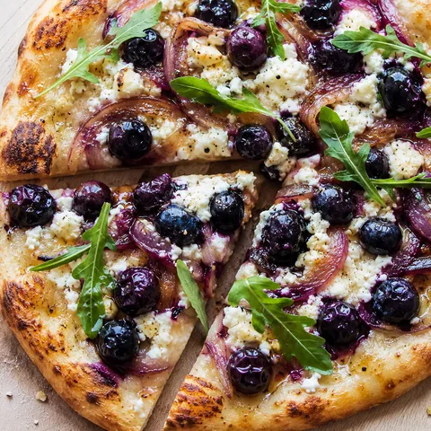 Blueberry feta honey naan pizza with arugula on a wooden board