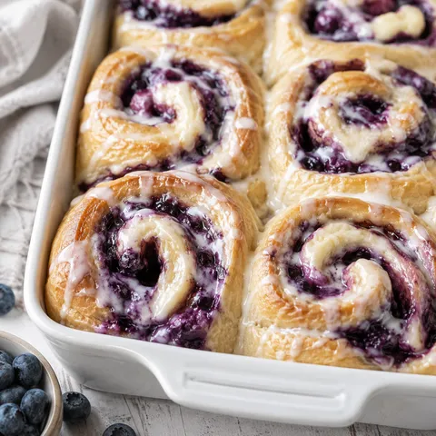 Blueberry cheesecake swirl rolls with vanilla glaze in a white baking dish