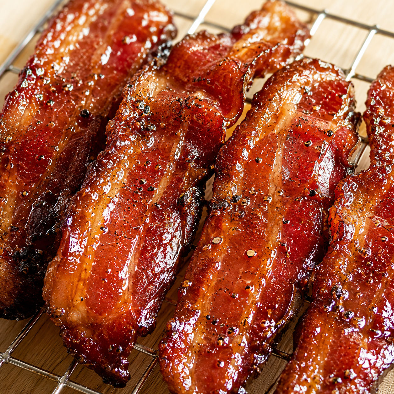 Candied bourbon maple bacon strips with a glossy sweet glaze on a wire rack
