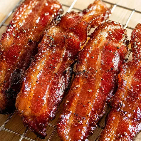 Candied bourbon maple bacon strips with a glossy sweet glaze on a wire rack