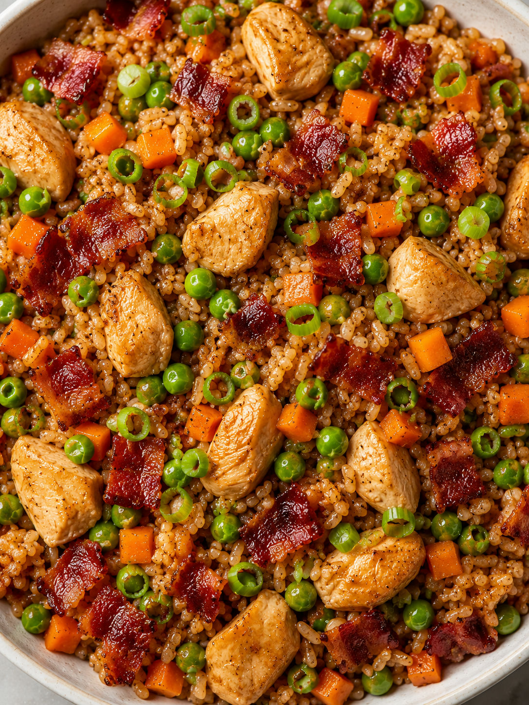 Overhead bowl of chicken and bacon fried rice with peas, carrots, and green onions