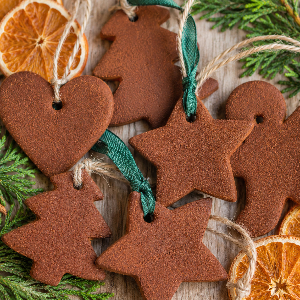 Cinnamon ornaments tied with ribbon beside dried orange slices and evergreen