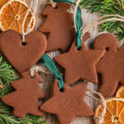 Cinnamon ornaments tied with ribbon beside dried orange slices and evergreen