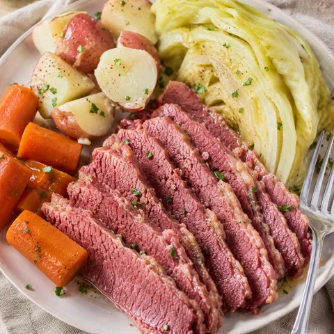 Sliced corned beef and cabbage with potatoes and carrots on a white plate