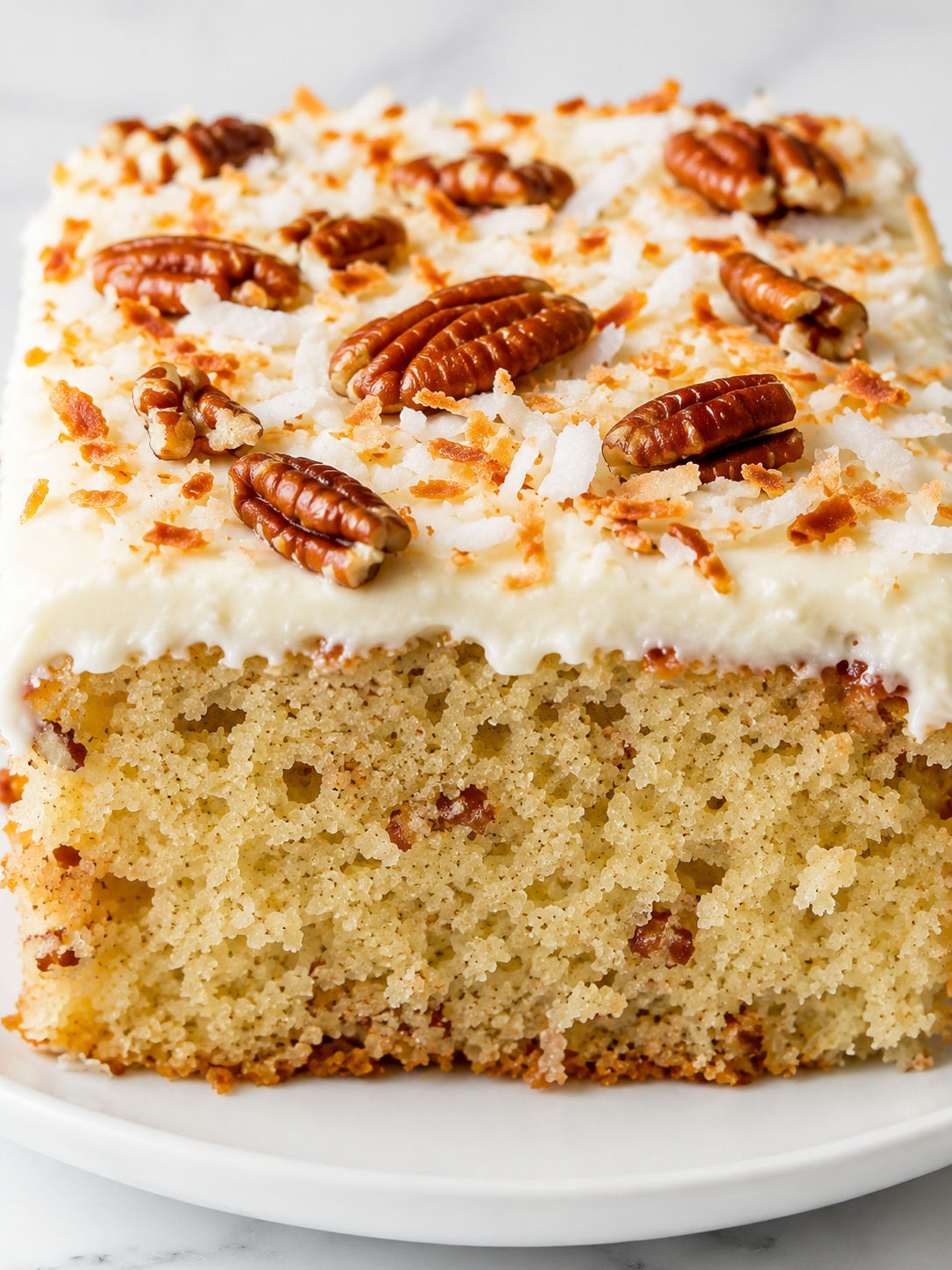 Tall slice of coconut pecan buttermilk cake with creamy frosting