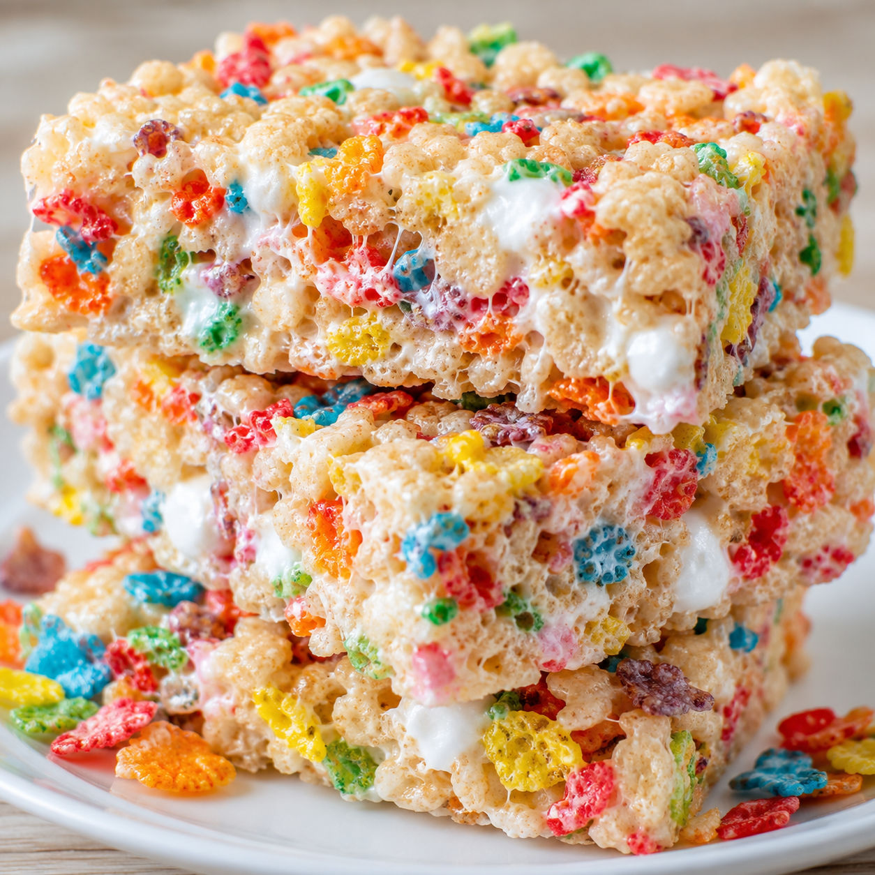 Colorful Fruity Pebbles Krispie Treats stacked on a white plate
