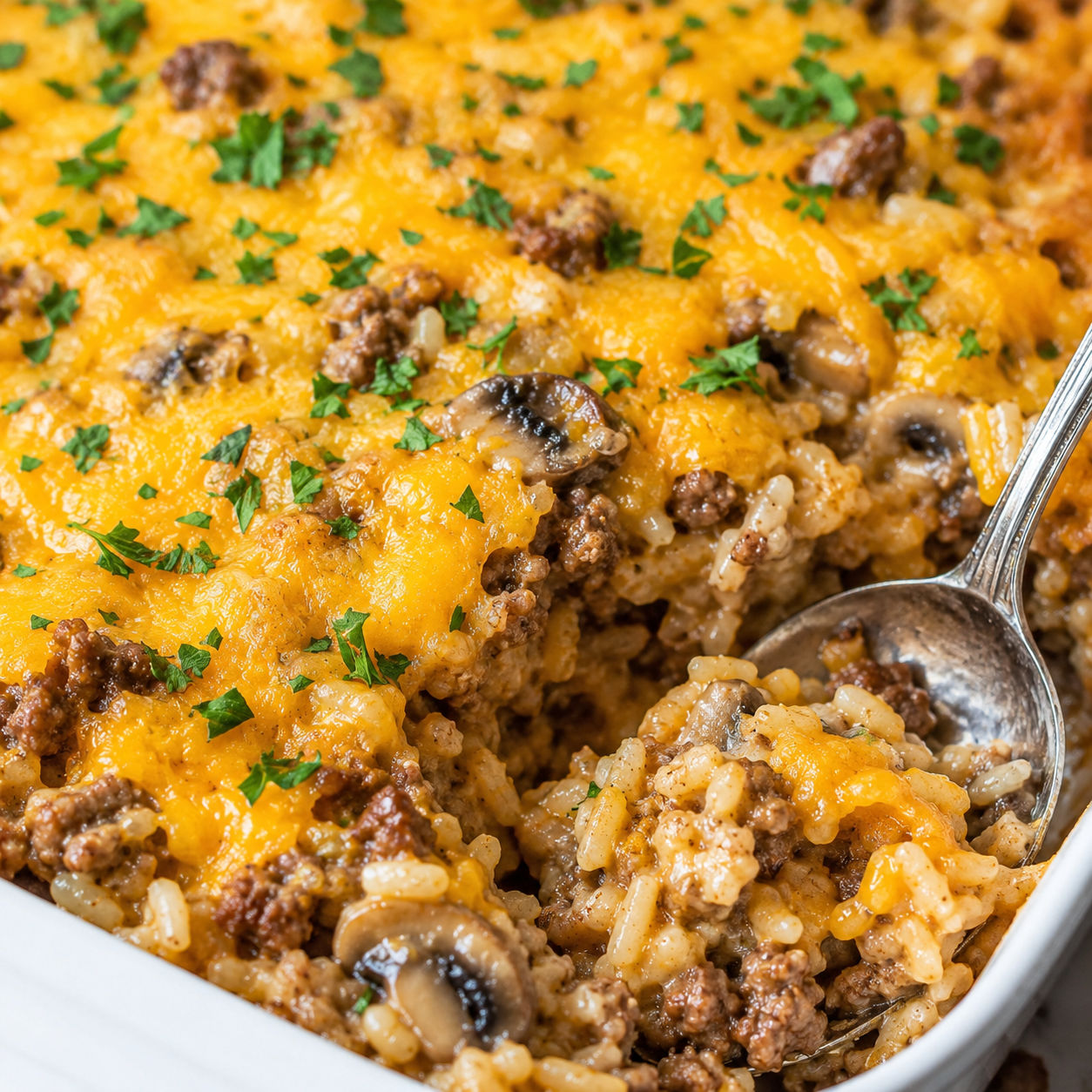 Beef and rice casserole with melted cheddar and parsley in a white dish