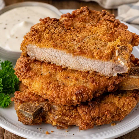 Golden country fried pork chops with crispy seasoned crust on a white plate