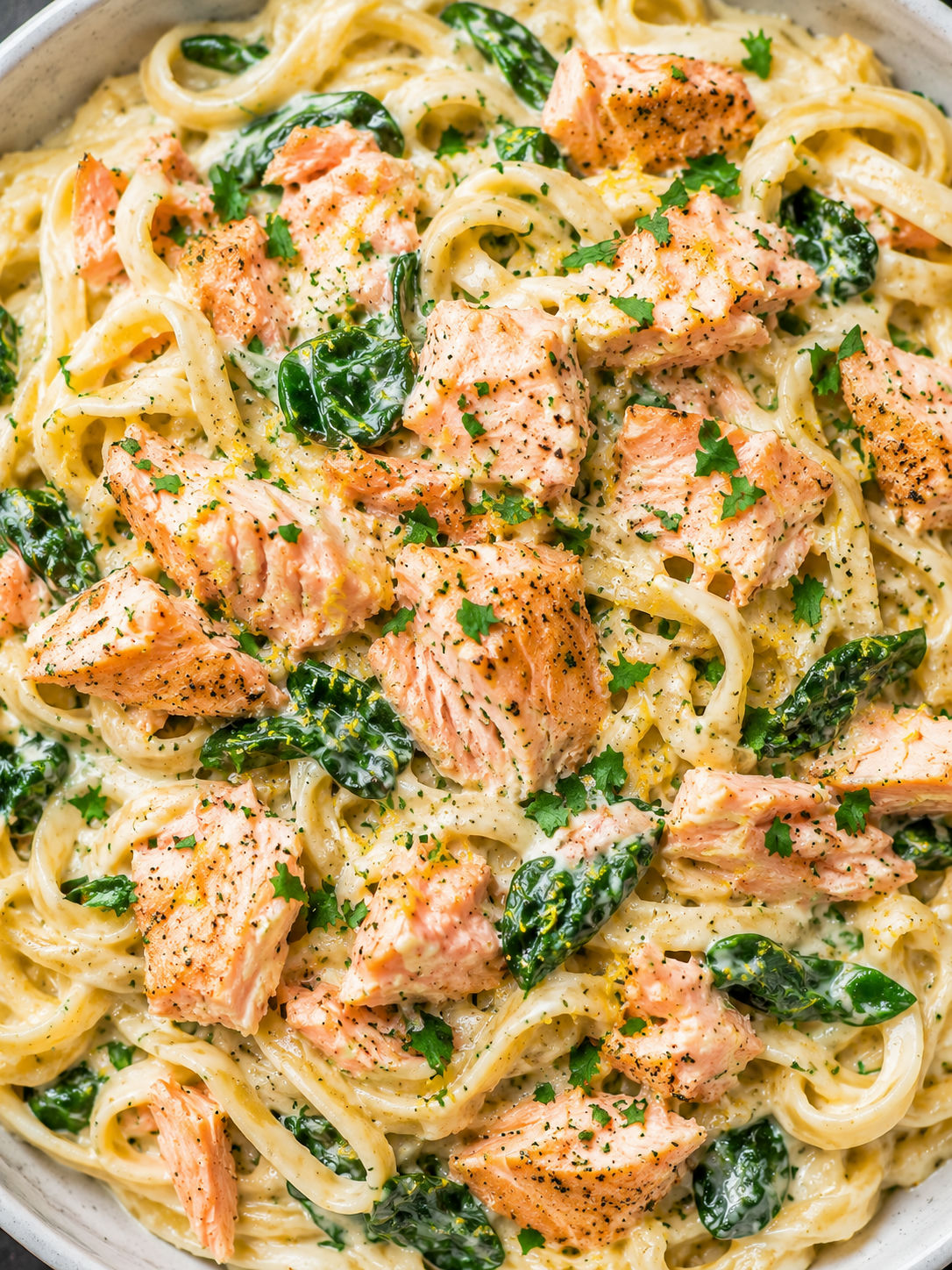 Creamy garlic salmon pasta filling the frame with spinach, parsley, and lemon