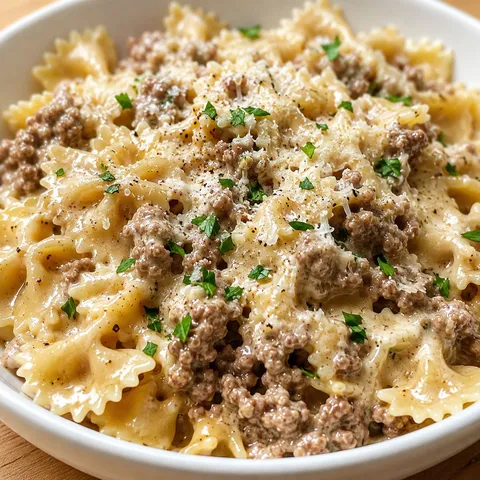 Creamy Parmesan bowtie pasta with ground beef and parsley in a white bowl
