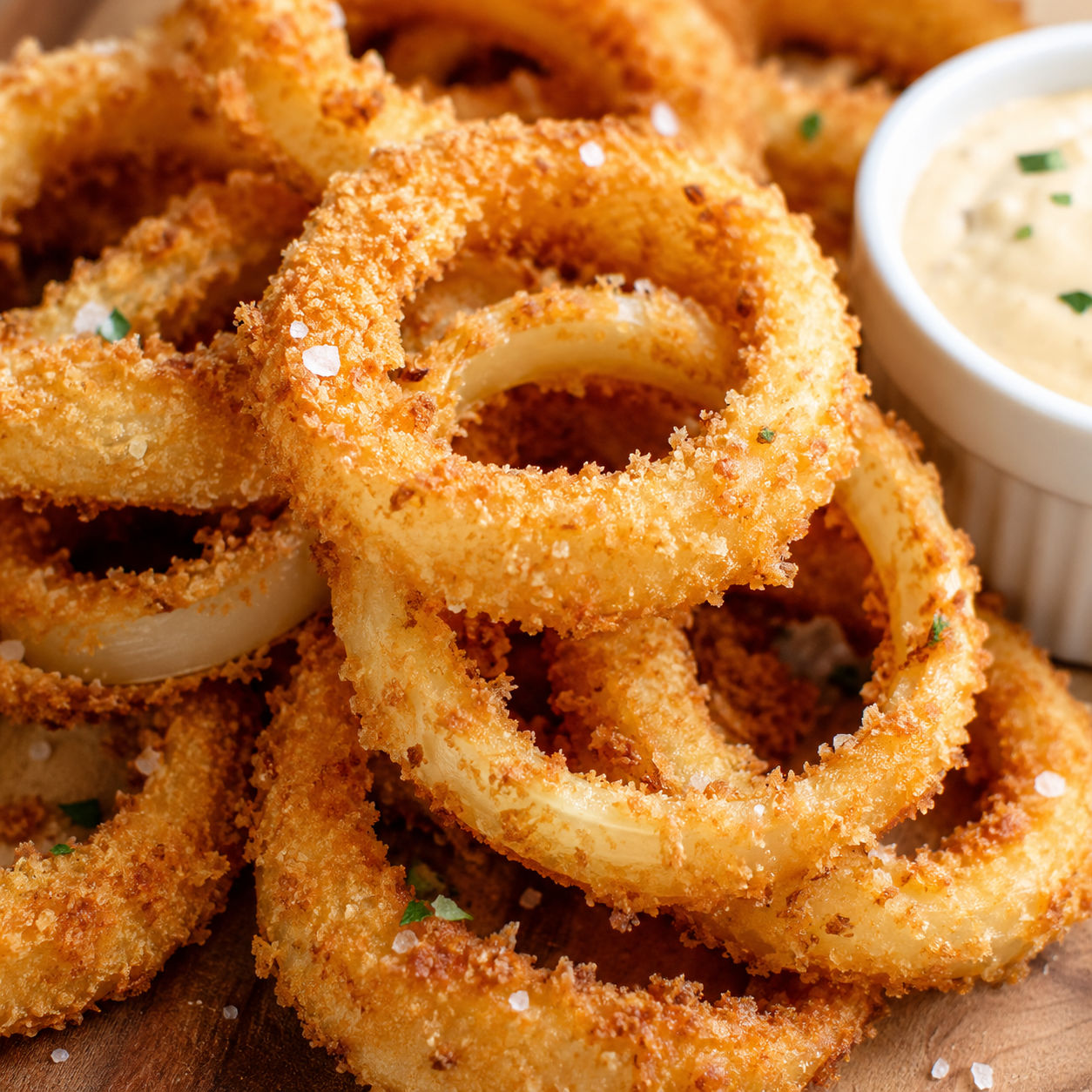Golden panko onion rings with creamy dipping sauce on a wood table