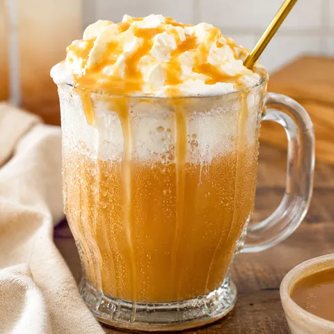 Frosty mug of homemade butterbeer with whipped cream and butterscotch drizzle
