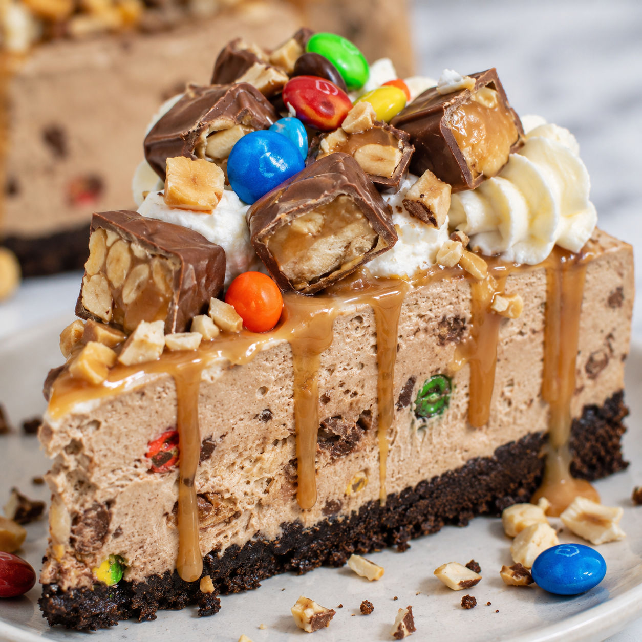 M&M Snickers cheesecake slice with caramel, whipped cream, and peanuts