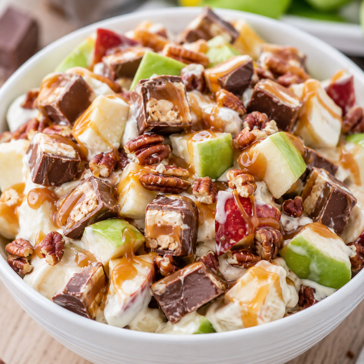 Snickers salad with apples, caramel drizzle, and chopped candy in a white bowl