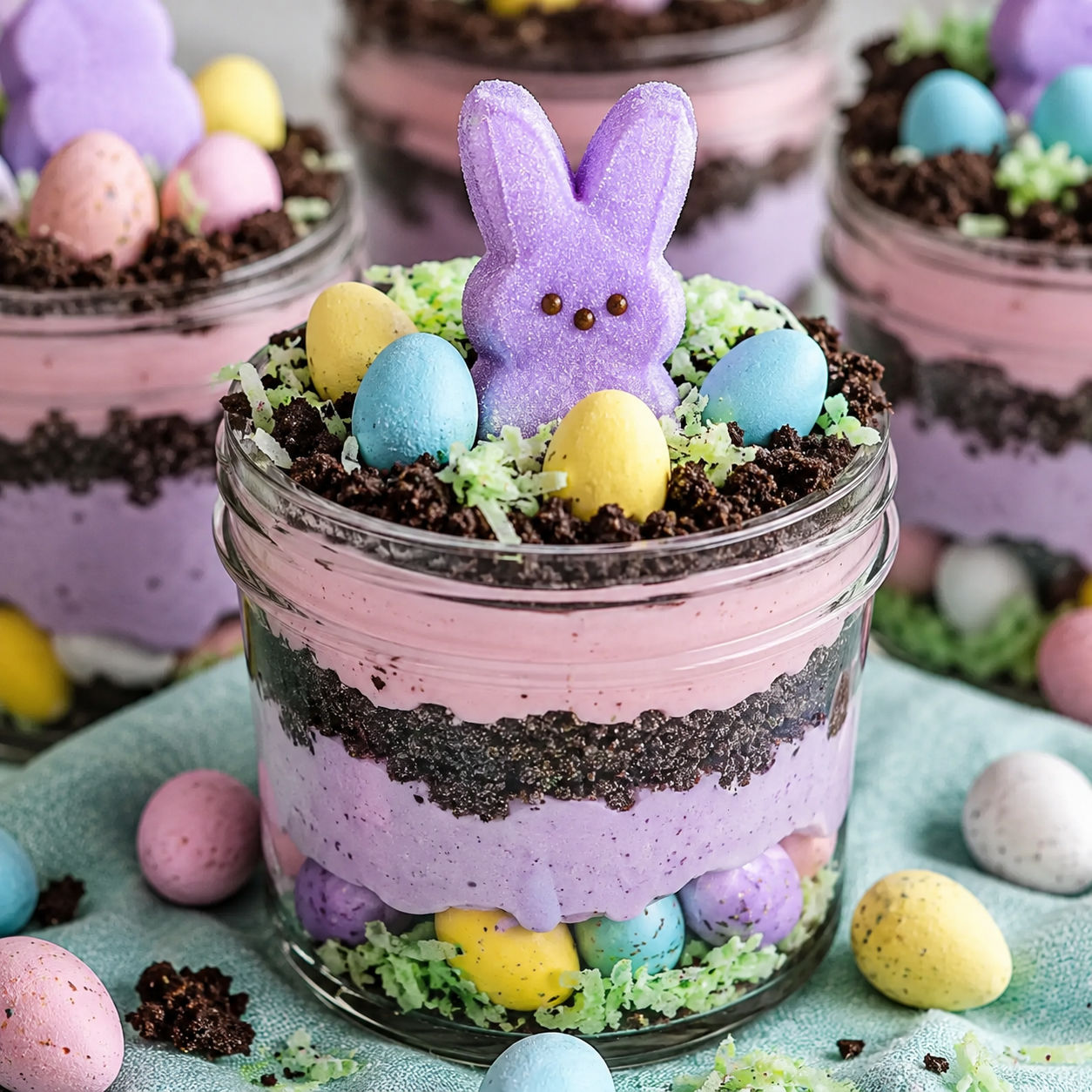 Easter dirt pudding jars with pastel pudding, Oreo crumbs, candy eggs, and Peeps
