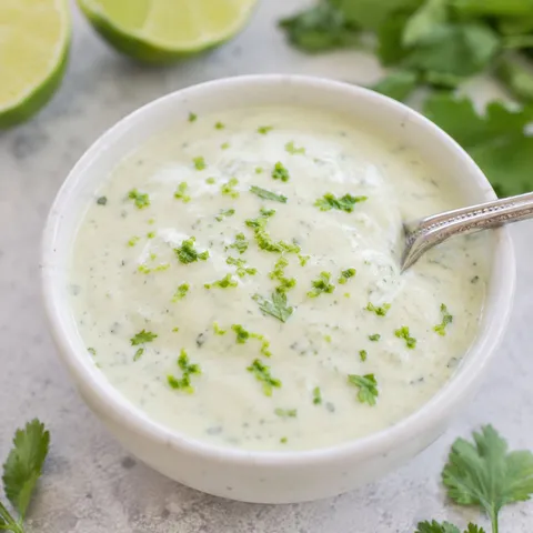 Cilantro lime crema in a white bowl with lime and cilantro