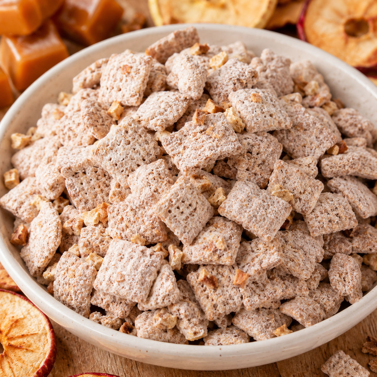 Caramel apple puppy chow in a cream bowl with apple chips