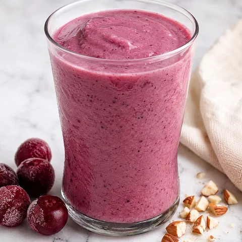 Creamy cherry smoothie in a glass with frozen cherries and almonds
