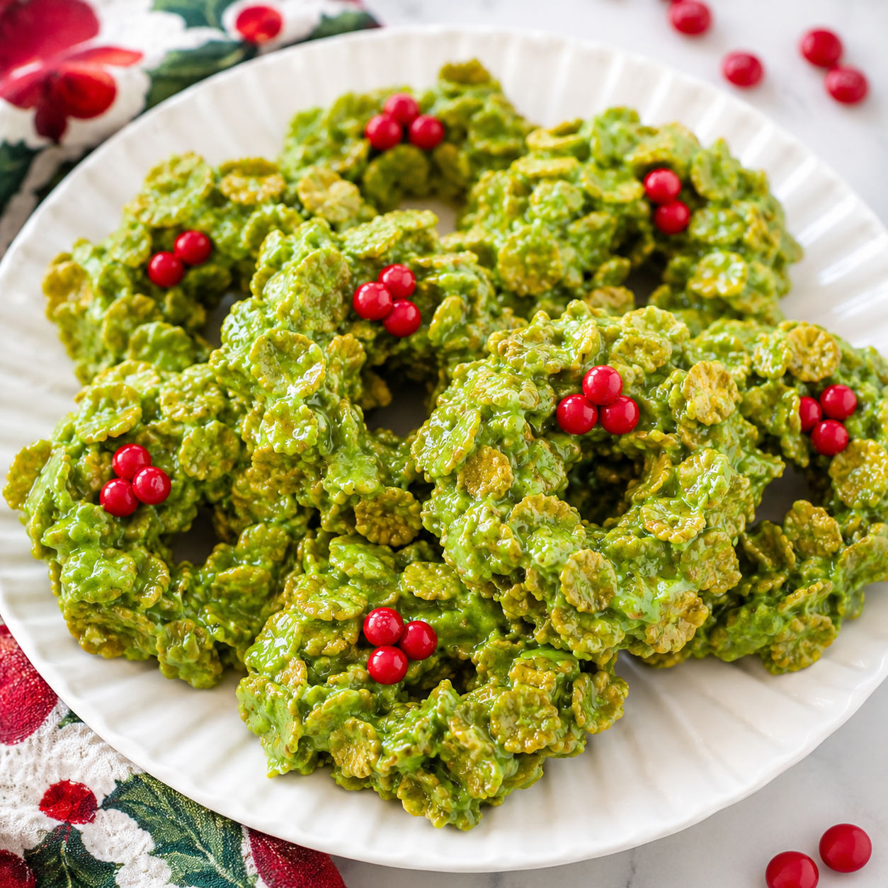Green cornflake wreath treats with red candy berries on a white platter
