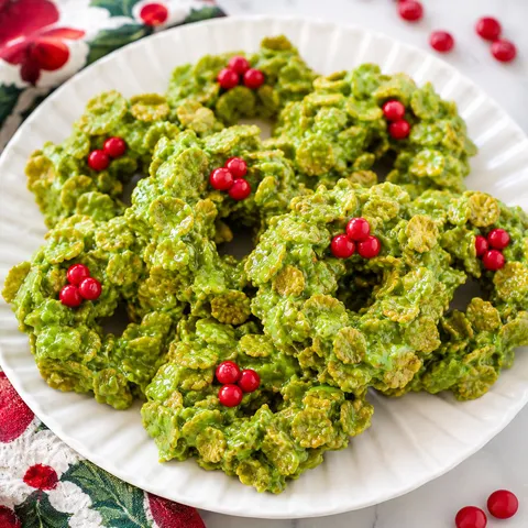 Green cornflake wreath treats with red candy berries on a white platter