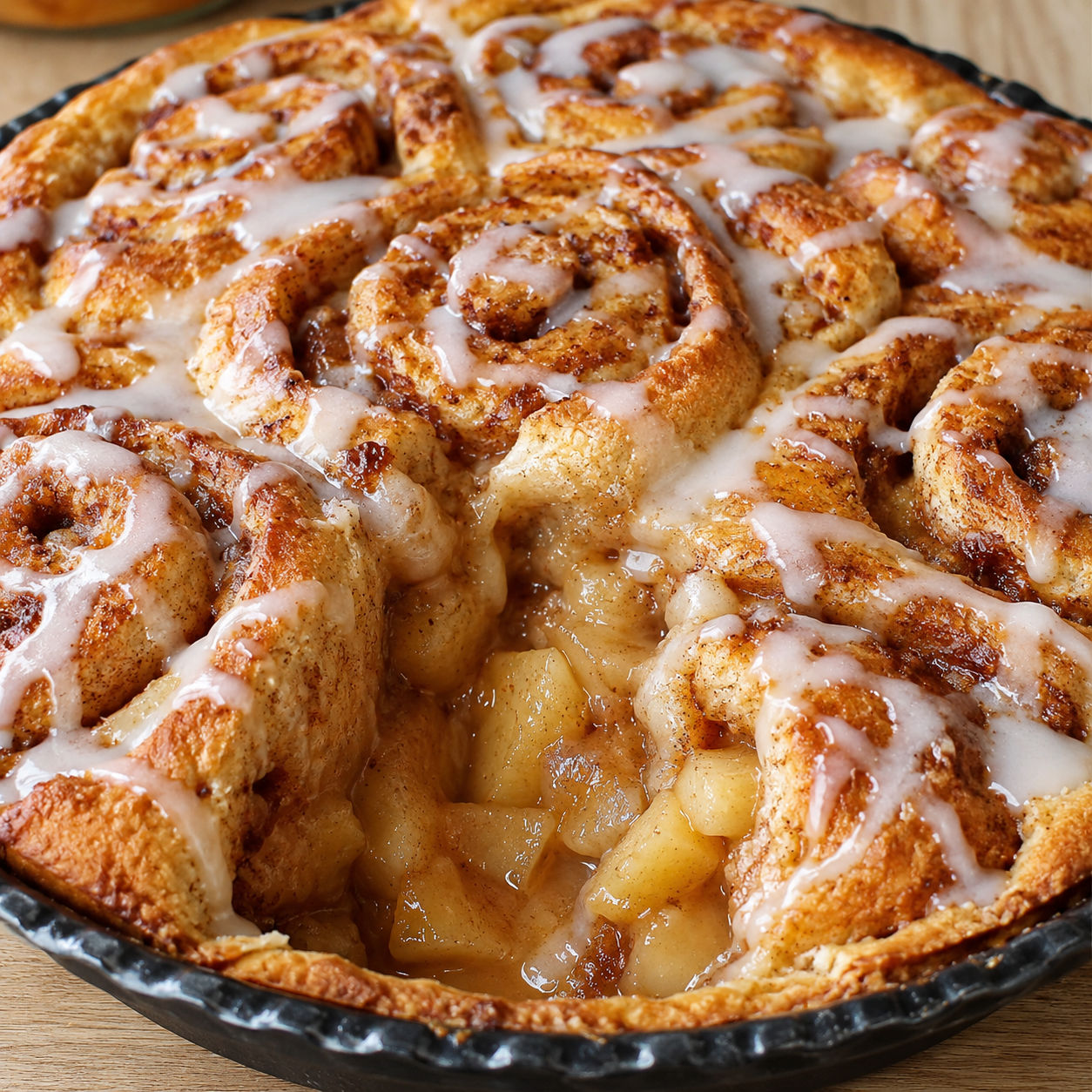Baked cinnamon roll apple pie with golden crust and white icing drizzle