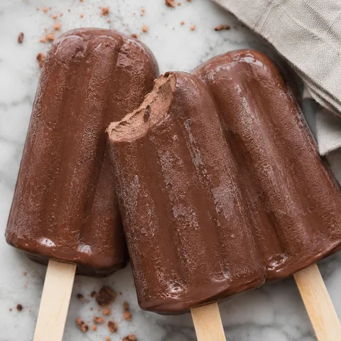 Creamy chocolate popsicles with a fudgy bitten center on marble