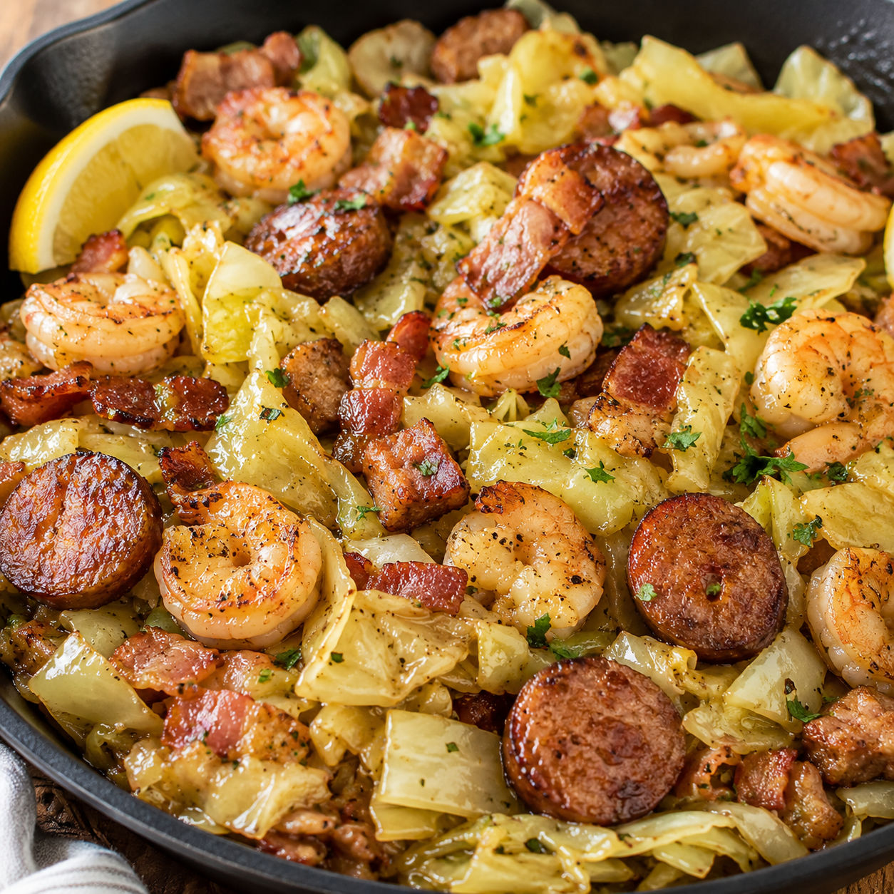 Fried cabbage with shrimp, sausage, and bacon in a cast iron skillet with lemon