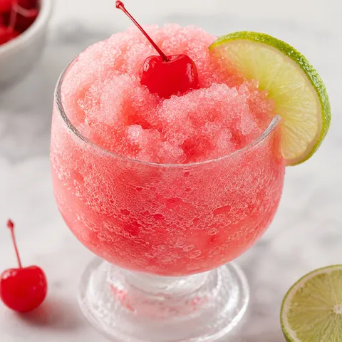 Frozen Shirley Temple mocktail with cherry and lime in a frosty glass