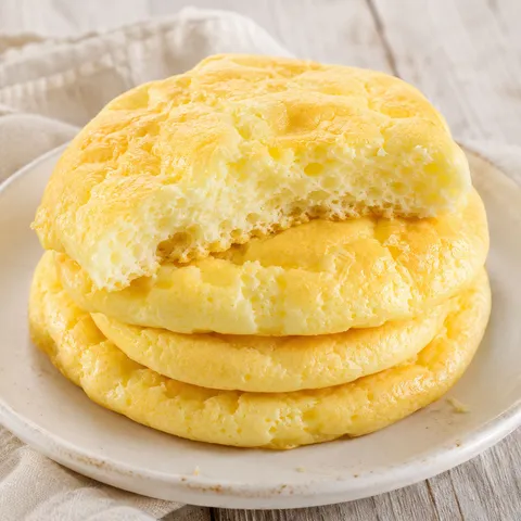 Golden keto cloud bread rounds stacked with one torn open