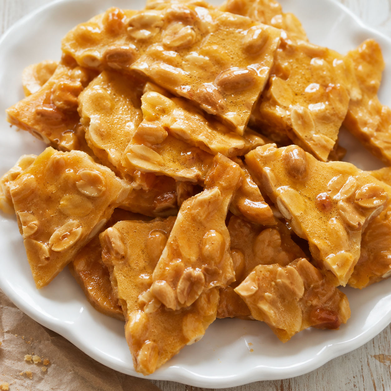 Golden microwave peanut brittle shards with roasted peanuts on a white plate