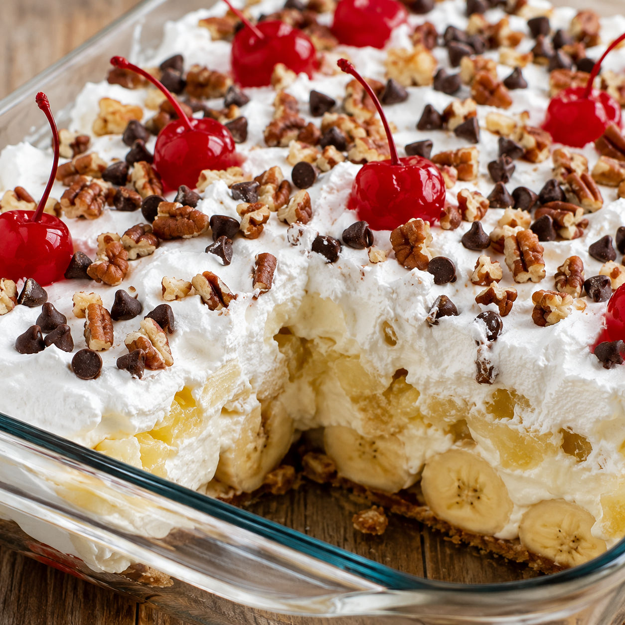 No-bake banana split cake with whipped topping, pecans, chocolate chips, and cherries