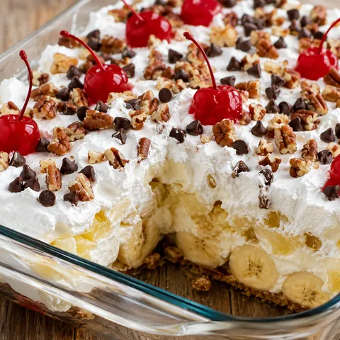 No-bake banana split cake with whipped topping, pecans, chocolate chips, and cherries