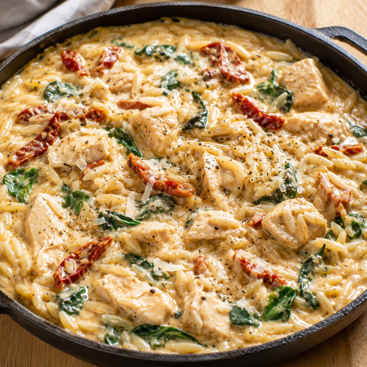 Creamy marry me chicken orzo with spinach and sun-dried tomatoes in a skillet