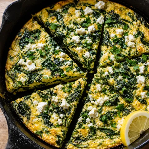 Spinach feta frittata wedges in a skillet with parsley and lemon