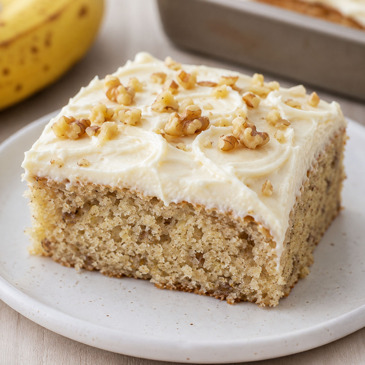 Banana cake slice with cream cheese frosting and chopped walnuts