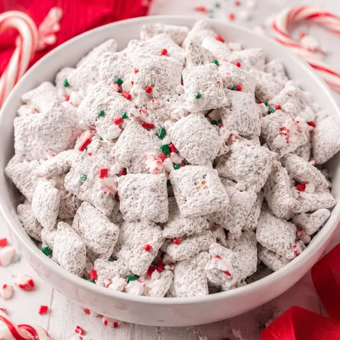 Peppermint candy cane puppy chow in a white bowl with red candy flecks