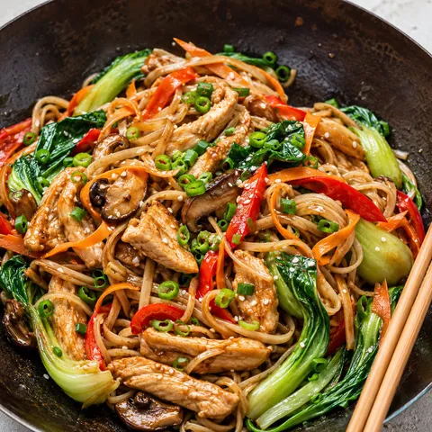 Chicken stir fry with rice noodles, vegetables, green onions, and sesame seeds