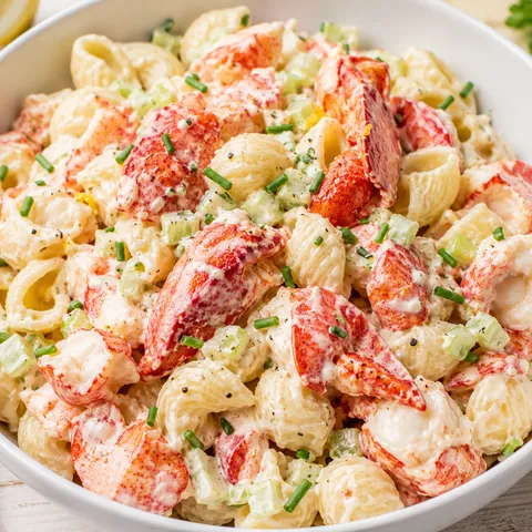 Lobster roll pasta salad with creamy dressing and chives in a white bowl