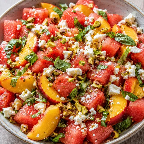 Watermelon peach feta salad with basil and pistachios in a ceramic bowl