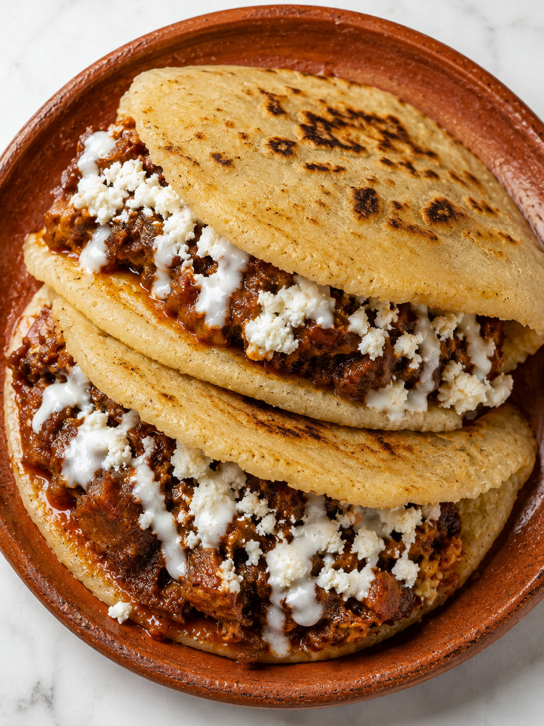 Two gorditas filled with chicharron en salsa and queso fresco on a rustic clay plate with lime
