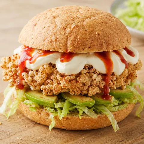 Crispy chicken sandwich with avocado, lettuce, yogurt dressing, and hot sauce