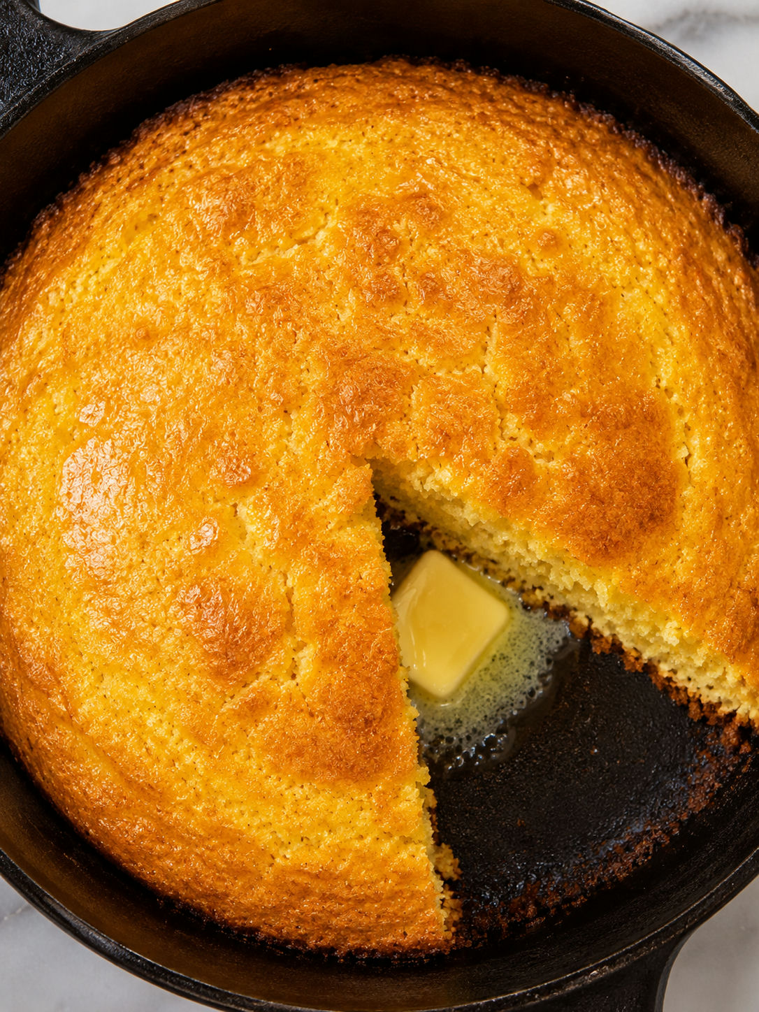 Overhead view of golden Southern buttermilk cornbread in a cast iron skillet with a wedge removed showing the moist crumb