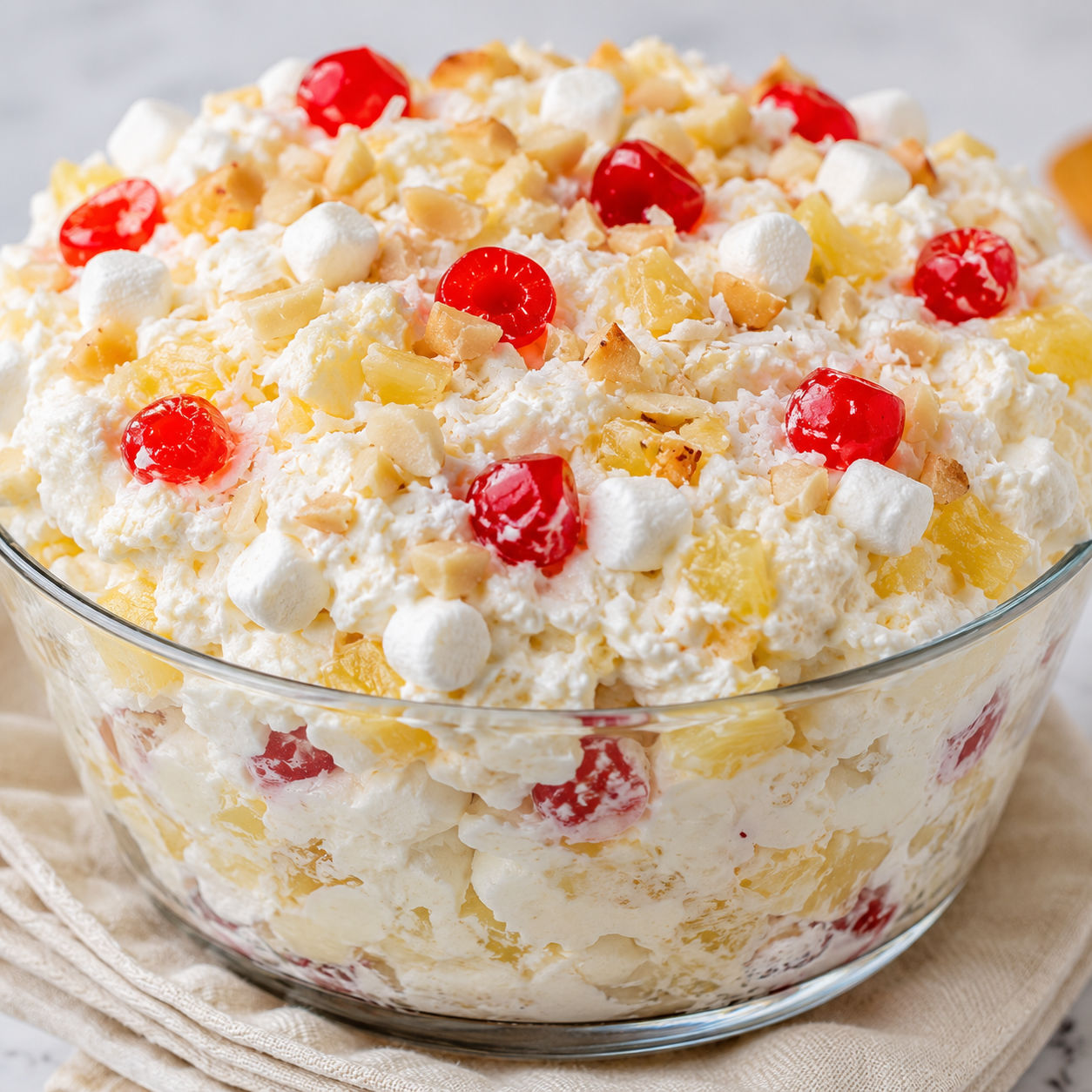 Hawaiian pineapple coconut fluff dessert in a glass trifle bowl with cherries and nuts