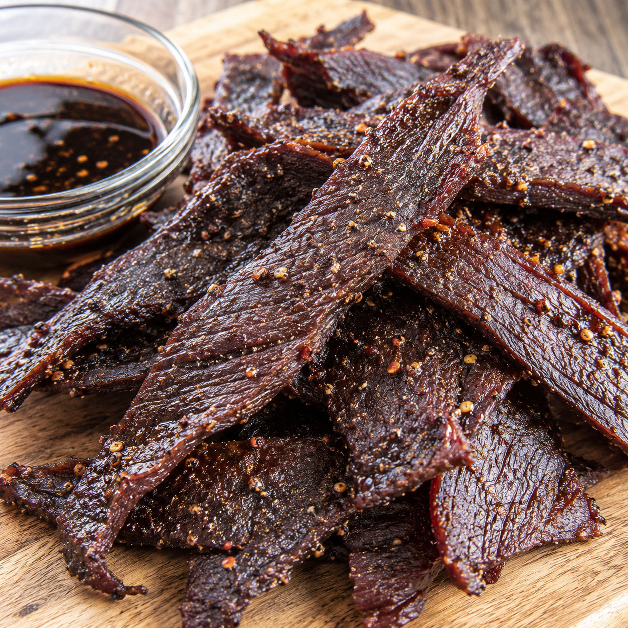 Homemade air fryer beef jerky strips with black pepper on a wooden board