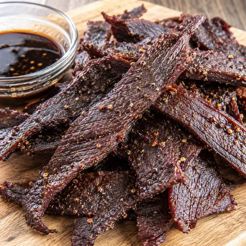 Homemade air fryer beef jerky strips with black pepper on a wooden board